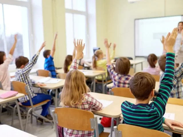 group-of-school-kids-raising-hands-in-classroom-920x600