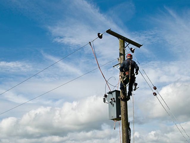 An unrecognisable utility workman carries out repairs on a transformer connected to an 11000 volt power line.