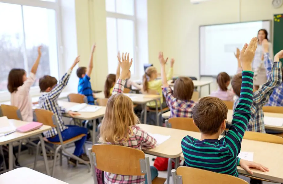 group-of-school-kids-raising-hands-in-classroom-920x600
